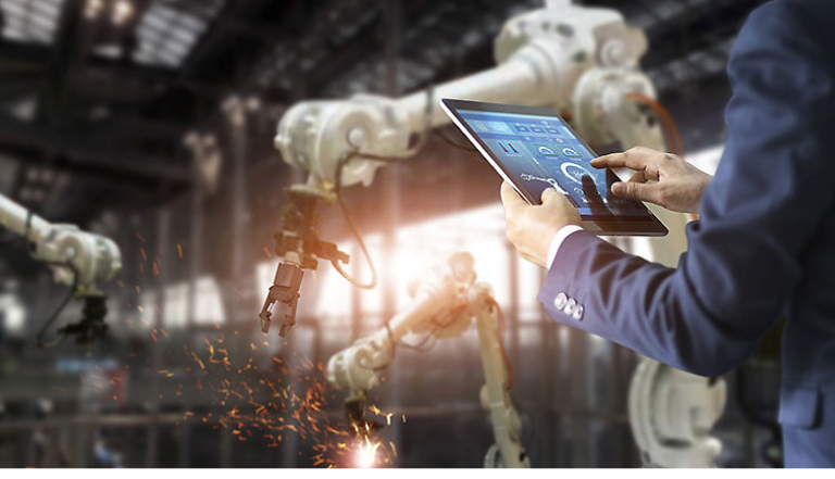 arms of a person in a suit hold a tablet out, three white robotic arms are seen working behind the tablet, with orange sparks flying from beneath the arms